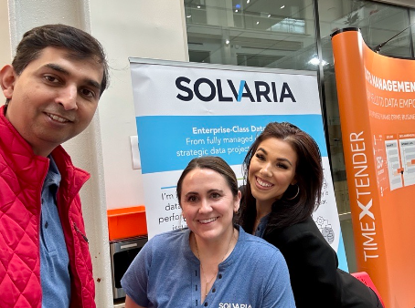 Three people smiling in front of a SolAria banner, capturing a joyful moment of togetherness.