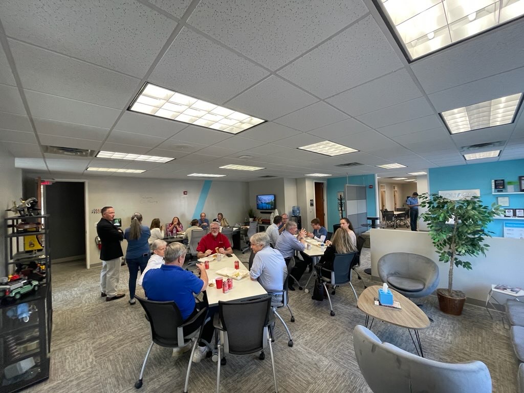 A diverse group of professionals engaged in work discussions at tables in a modern office setting.