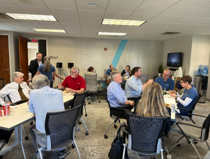 Multicultural team sitting at tables in an office, engaged in a meeting or discussion.